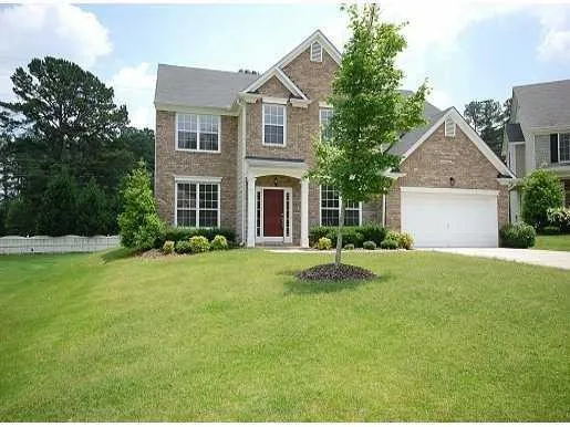 Brick Colonial-style residence featuring a symmetrical façade with multiple windows, a covered entry portico with red door, and a two-car garage