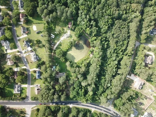 Aerial view showcasing a substantial land parcel featuring a central pond, bordered by extensive mature tree coverage