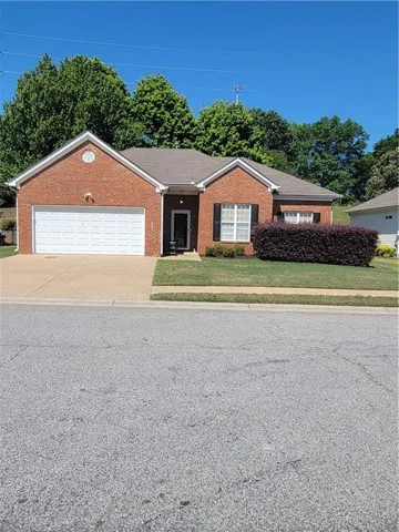 Brick-clad single-story residence featuring an attached two-car garage, mature landscaping, and a covered entryway