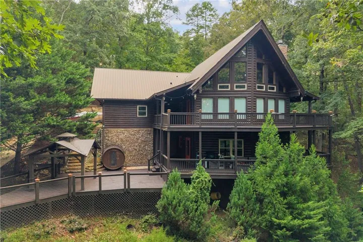 Log cabin exterior featuring a metal roof, stone foundation, multi-level decks, and a prominent gable with large windows