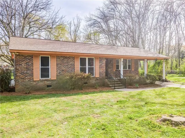 Brick exterior featuring a covered front porch with white columns, a concrete walkway, and a landscaped foundation