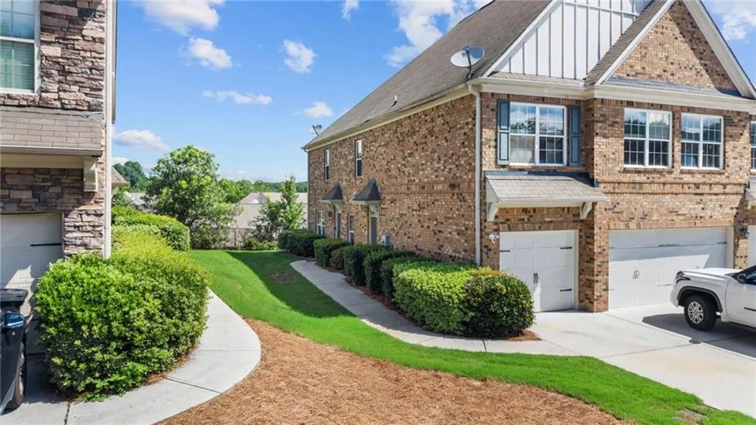 Brick and stone facade townhome featuring white garage doors and a gabled roofline