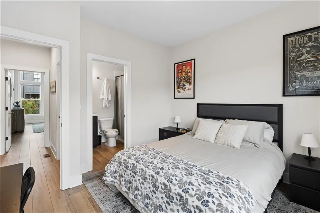 Bedroom featuring light-toned walls, wood-finish flooring, and an attached full bathroom