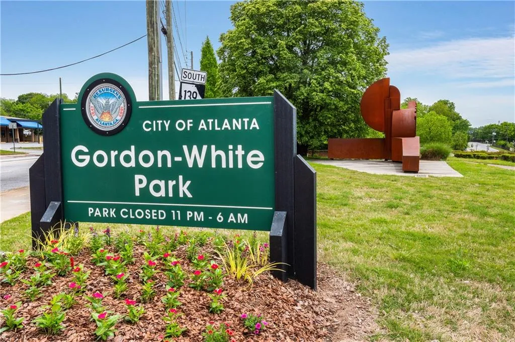 Gordon-White Park entrance signage featuring a City of Atlanta emblem, established landscaping, and a distant abstract metal sculpture