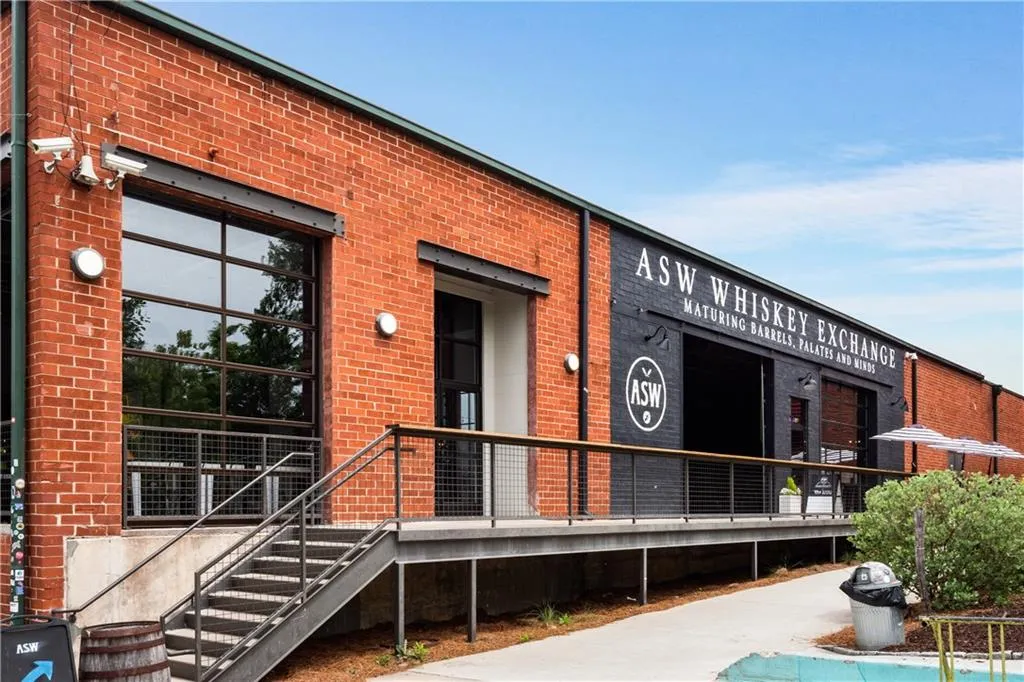 Industrial brick building featuring a large glass-paneled roll-up door, dark painted facade, metal stairs, and an elevated metal walkway with railings