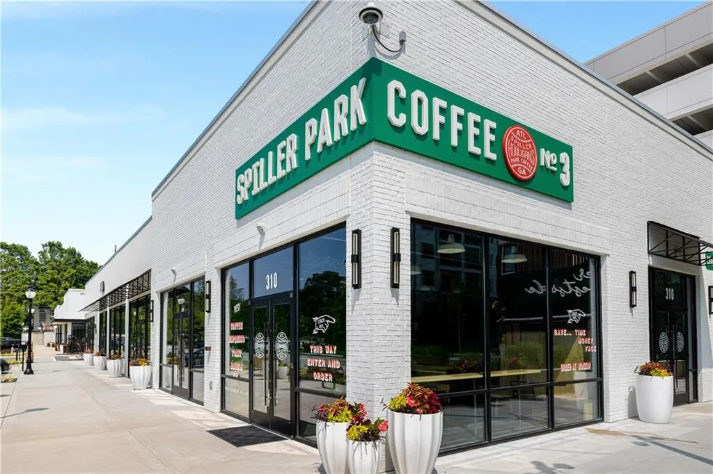 Commercial storefront featuring a bright white brick exterior, large glass pane windows, a prominent green and red business sign, and modern black sconce lighting