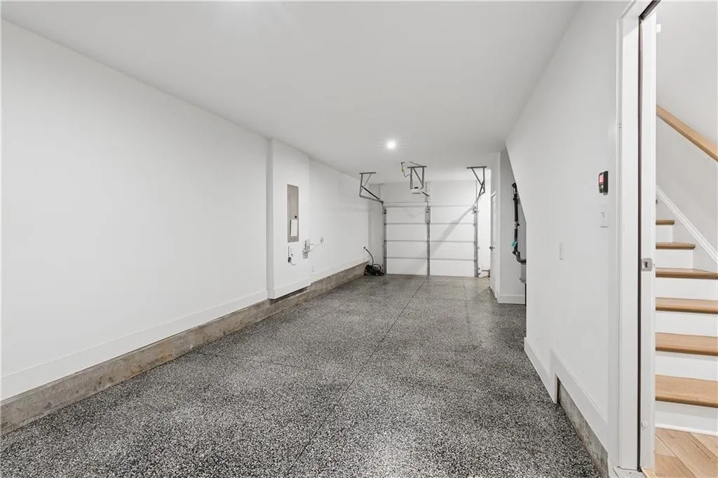 Spacious garage with an epoxy-coated concrete floor, white painted walls, recessed lighting, and direct access to a natural wood staircase with white risers