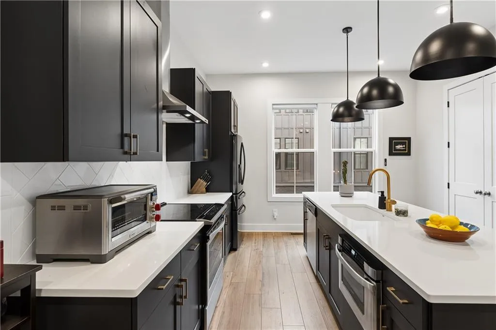 Modern kitchen featuring dark cabinetry, white countertops, a large island with an undermount sink, brass-finish faucet, and stainless steel appliances