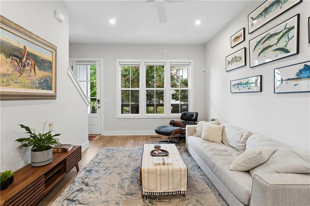 Spacious living area featuring light wood-finish flooring, a contemporary ceiling fan, recessed lighting, and large windows providing ample natural light
