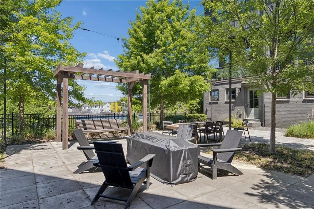 Paved patio area featuring mature trees, a wooden pergola, and a built-in wooden swing with water frontage