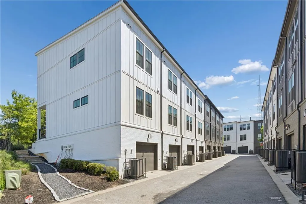 Modern townhome exterior featuring vertical white siding, black-framed windows, a garage door, and a white painted brick lower level