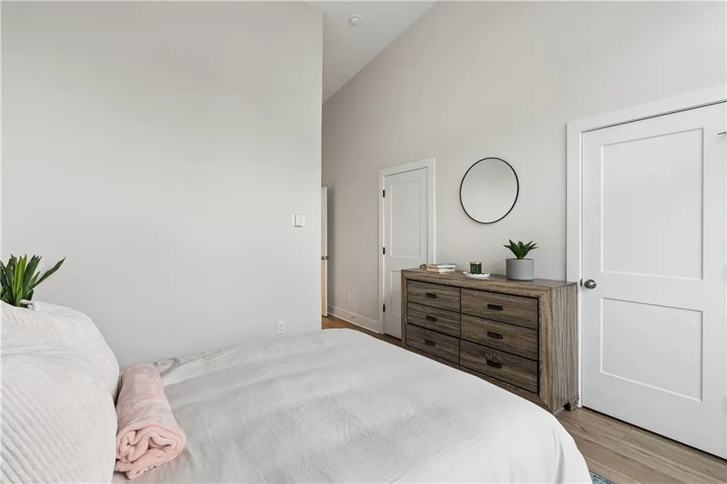 Vaulted ceiling bedroom featuring neutral wall tones, wood-finish flooring, and white panel doors