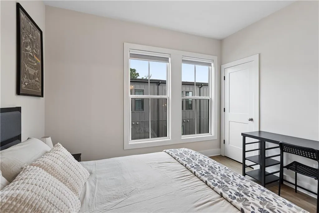 Bright room featuring two windows with white trim, wood-finish flooring, a white paneled door, and light neutral wall paint