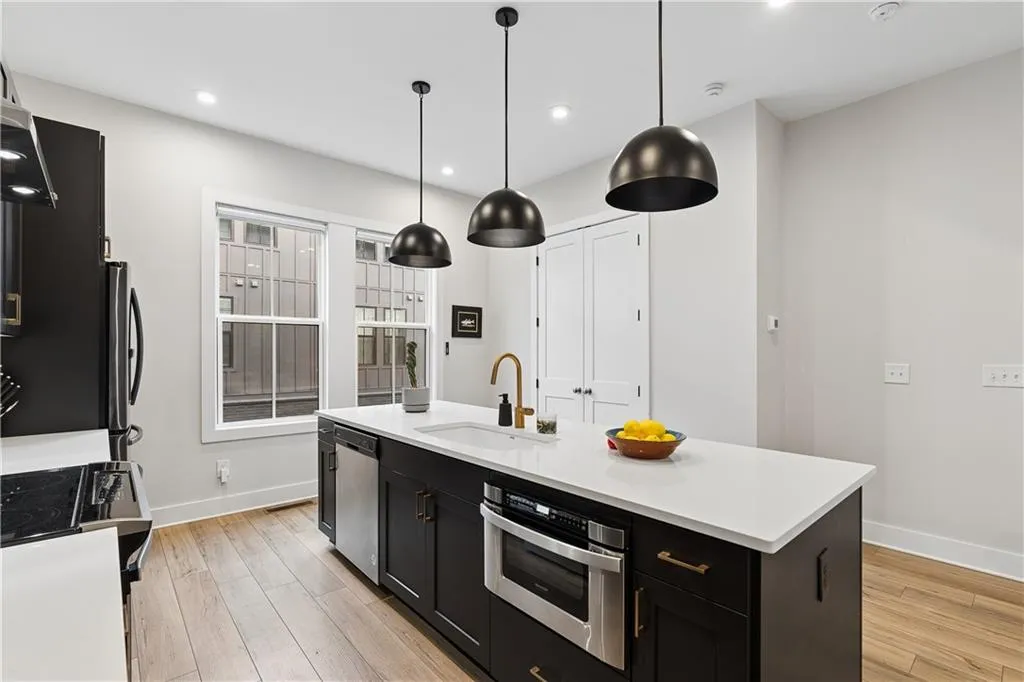Modern kitchen featuring a large central island with a white countertop and integrated sink, under-cabinet microwave, and dark cabinetry