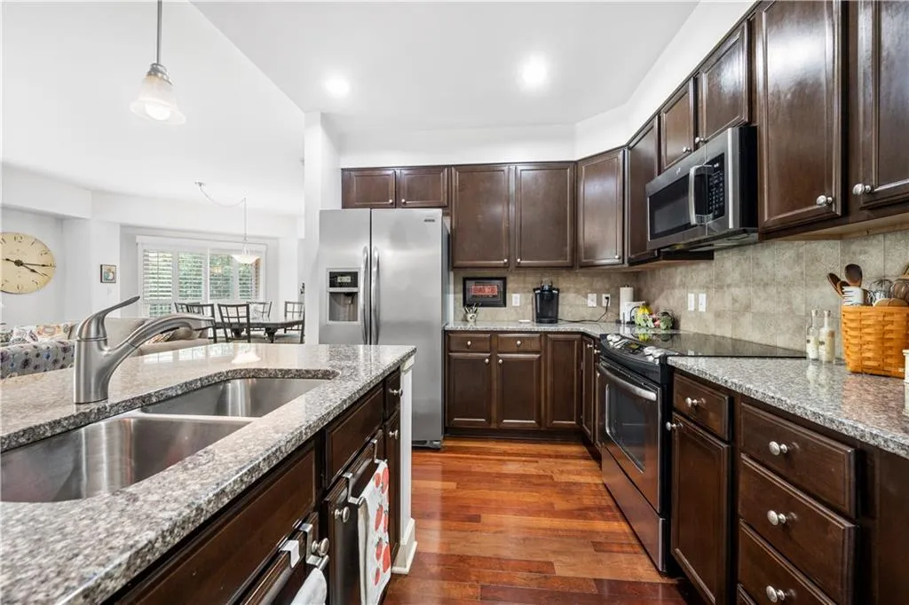 Kitchen featuring appliances with stainless steel finishes, a sink, dark wood finished floors, light stone countertops, and dark brown cabinetry