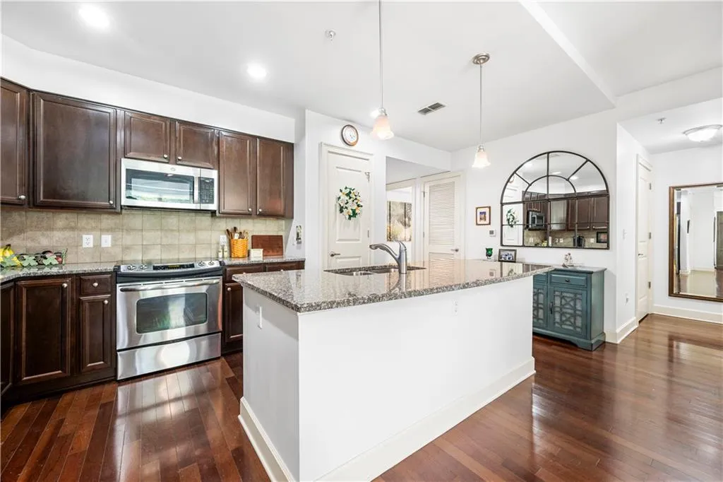 Kitchen featuring appliances with stainless steel finishes, a sink, dark wood finished floors, light stone countertops, and dark brown cabinets