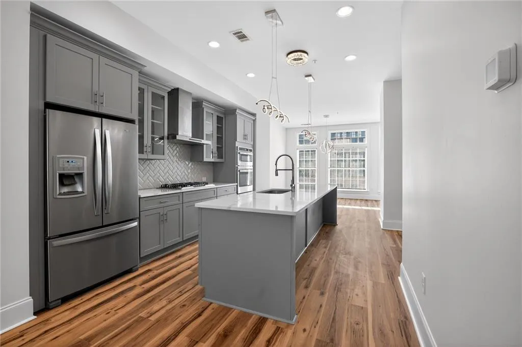 Kitchen featuring gray cabinets, glass fronted cabinets, stainless steel appliances, light stone counters, and decorative backsplash