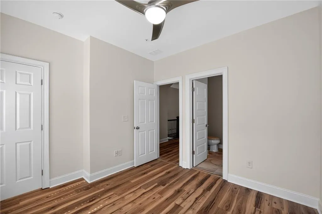 Unfurnished bedroom with dark wood-type flooring, ensuite bathroom, and ceiling fan