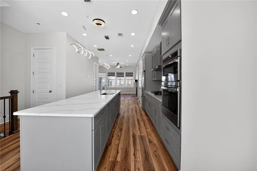 Kitchen featuring a spacious island, gray cabinets, light stone counters, stainless steel appliances, and dark wood-type flooring