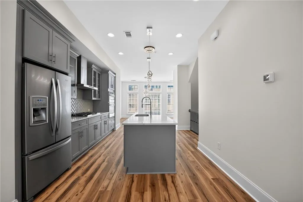 Kitchen with stainless steel appliances, a center island with sink, light stone countertops, gray cabinets, and pendant lighting