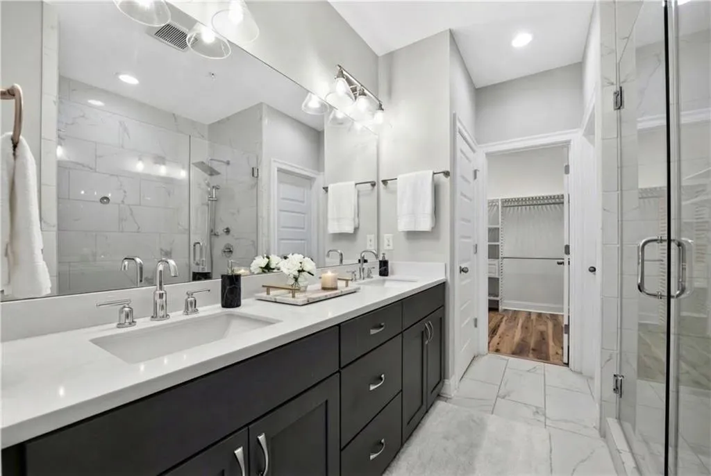 Full bath featuring double vanity, light marble finish floors, a marble finish shower, and a spacious closet