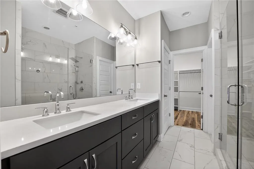 Bathroom featuring light marble finish floors, double vanity, a stall shower, and a spacious closet