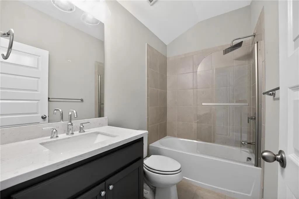 Full bath with vanity, lofted ceiling,  shower combination, and light tile patterned floors