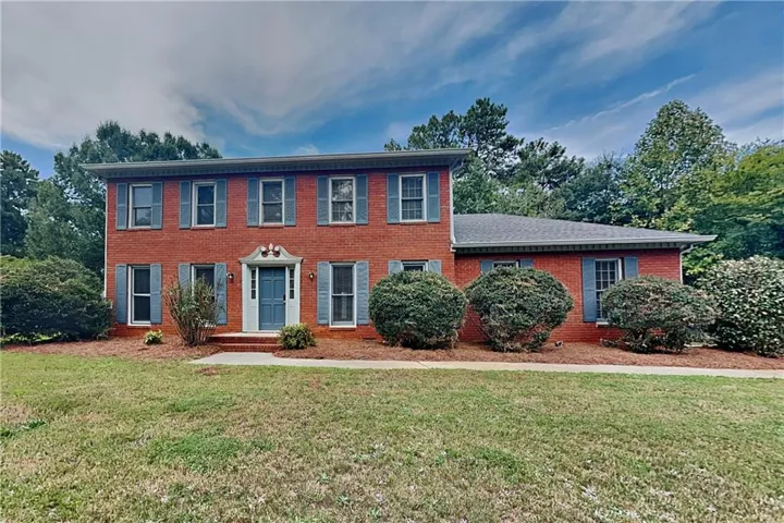 Brick exterior with gray shutters, featuring a light blue front door and mature landscaping