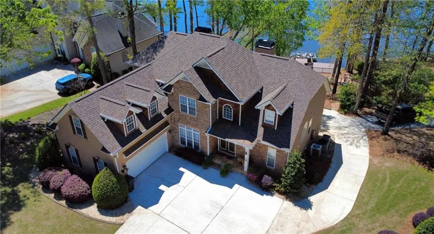 Brick and stucco exterior with multiple dormer windows, a two-car garage, established landscaping, and a private dock