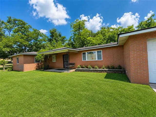 Brick exterior with a covered porch, an attached garage, and a separate structure, all set on a manicured lawn