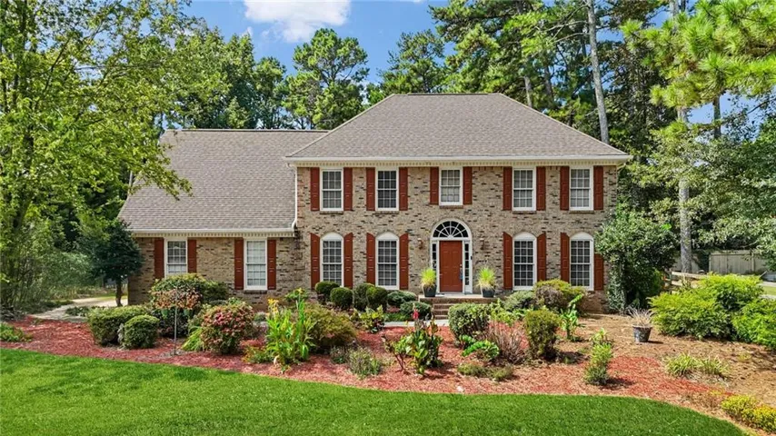 Two-story brick exterior with a gabled roof, individual pane windows, and dark red shutters