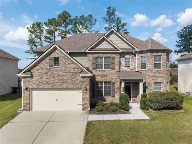Brick facade with shake siding accents, architectural shingle roof, two-car garage with carriage-style door, and mature landscaping