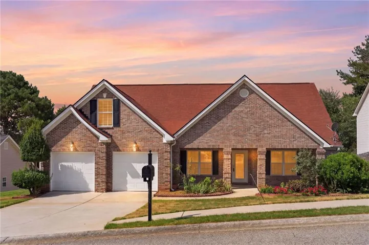 Brick Colonial home featuring a peaked gable roof with architectural detailing, two-car garage with paneled doors, and illuminated front windows