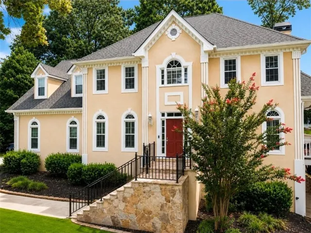 Stucco exterior with stone accents, a prominent red entry door, and dormer windows
