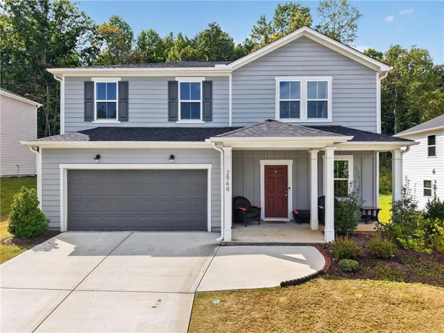 Two-story residence featuring light gray siding, a covered front porch with white columns, and a dark red entry door