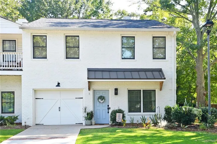 White brick exterior with black framed windows, a light blue entry door, an attached garage with a carriage-style door, and mature landscaping