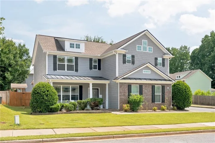 Two-story residence featuring a covered front porch, a combination of brick and siding exterior, black window shutters, and a dormer window