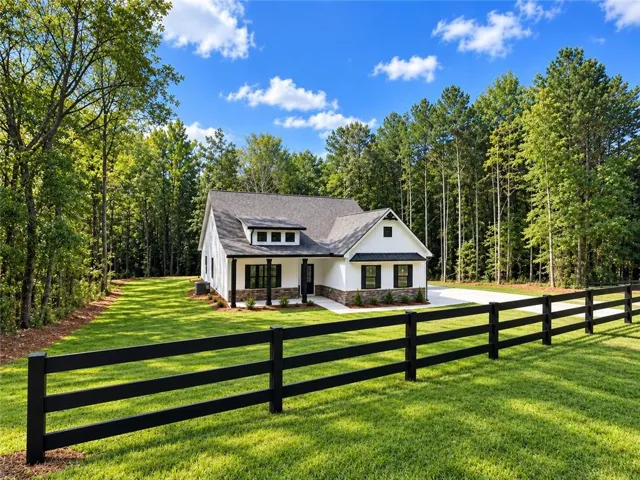 White exterior siding with dark shutters, gable roof, covered porch, and a black three-rail fence