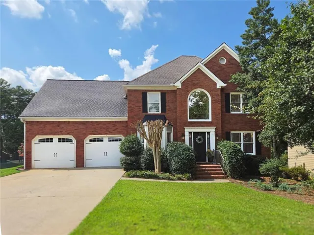 Brick exterior with a gabled roofline, arched window, and dual-car garage doors