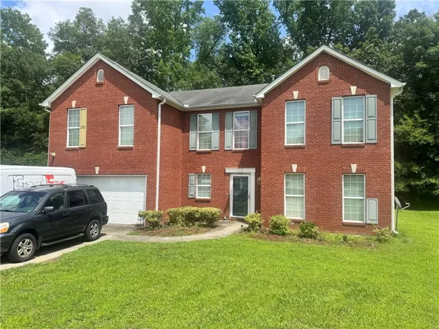 Two-story brick facade residence featuring a two-car garage, multiple windows with shutters, and a front entry