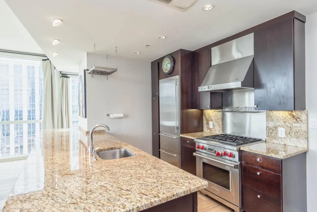 Kitchen with high end appliances, dark brown cabinets, light stone countertops, recessed lighting, and expansive windows