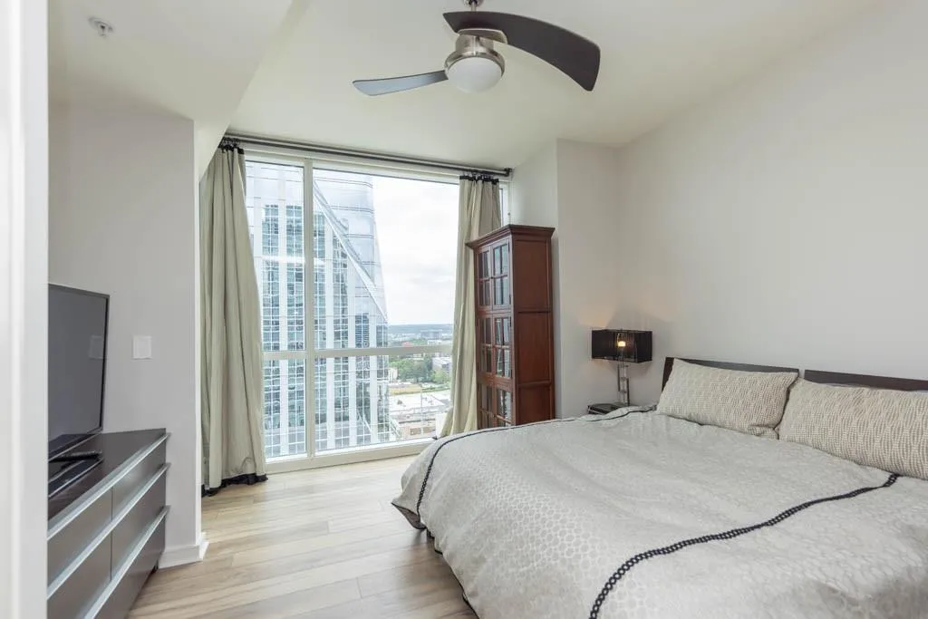 Bedroom with a wall of windows, light wood-style floors, a view of city, and ceiling fan