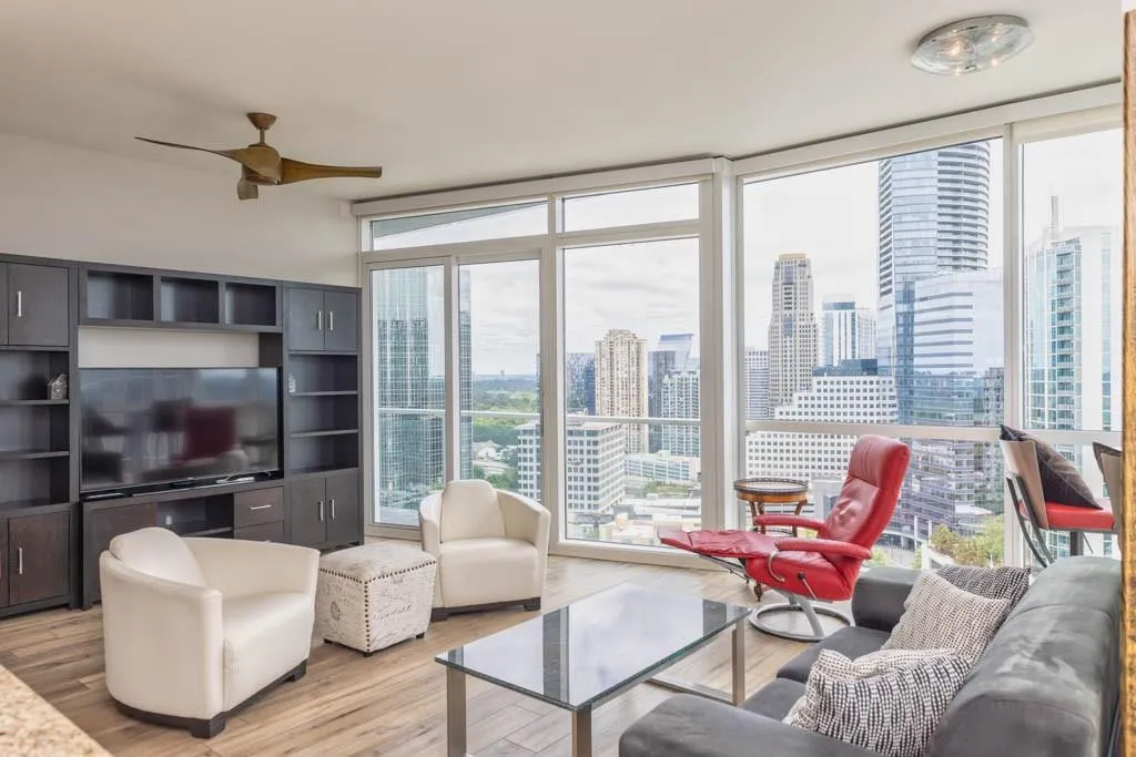 Living area with a wall of windows, light wood-style flooring, a skyline view, and a ceiling fan