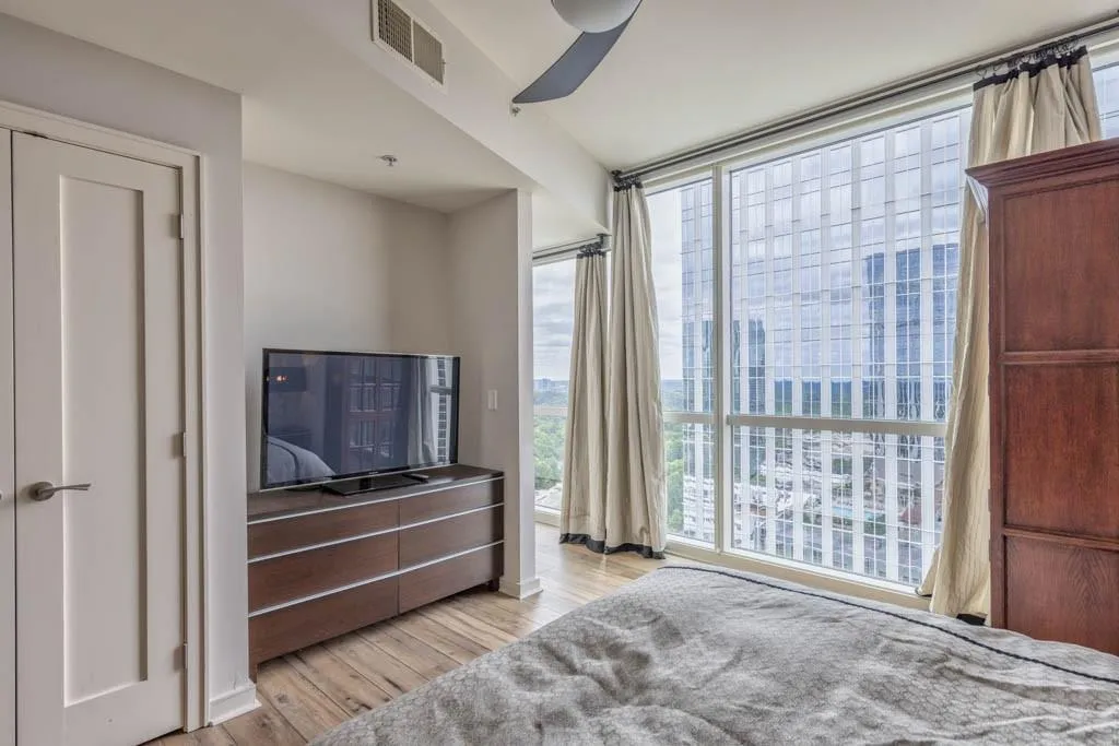 Bedroom with light wood-style flooring, a wall of windows, and a ceiling fan
