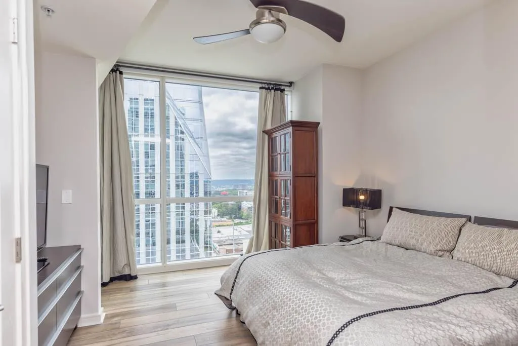 Bedroom with expansive windows, light wood-style floors, ceiling fan, and a city view