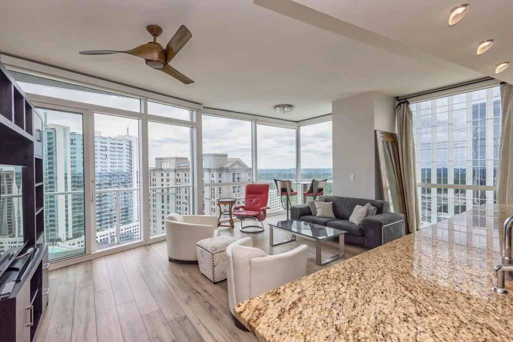 Living room featuring a wall of windows, light wood-style floors, a city view, and ceiling fan