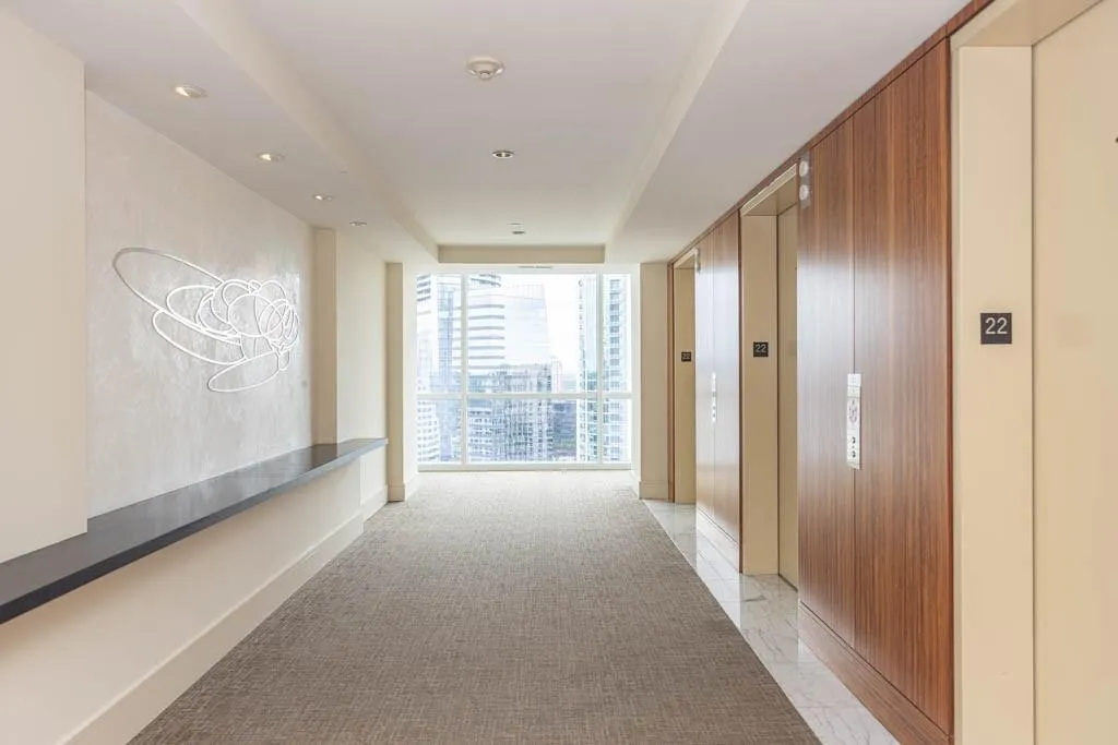 Hallway with a tray ceiling, elevator, floor to ceiling windows, recessed lighting, and light colored carpet