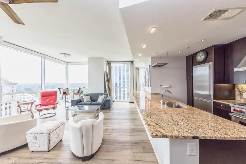 Kitchen featuring a wall of windows, dark brown cabinets, light stone countertops, high end fridge, and healthy amount of natural light