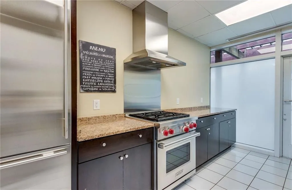 Kitchen featuring high end appliances, wall chimney exhaust hood, light tile patterned floors, a paneled ceiling, and light stone counters