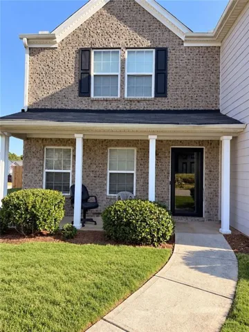 Brick facade with decorative shutters, covered front porch with white columns, concrete walkway, and landscaped shrubbery